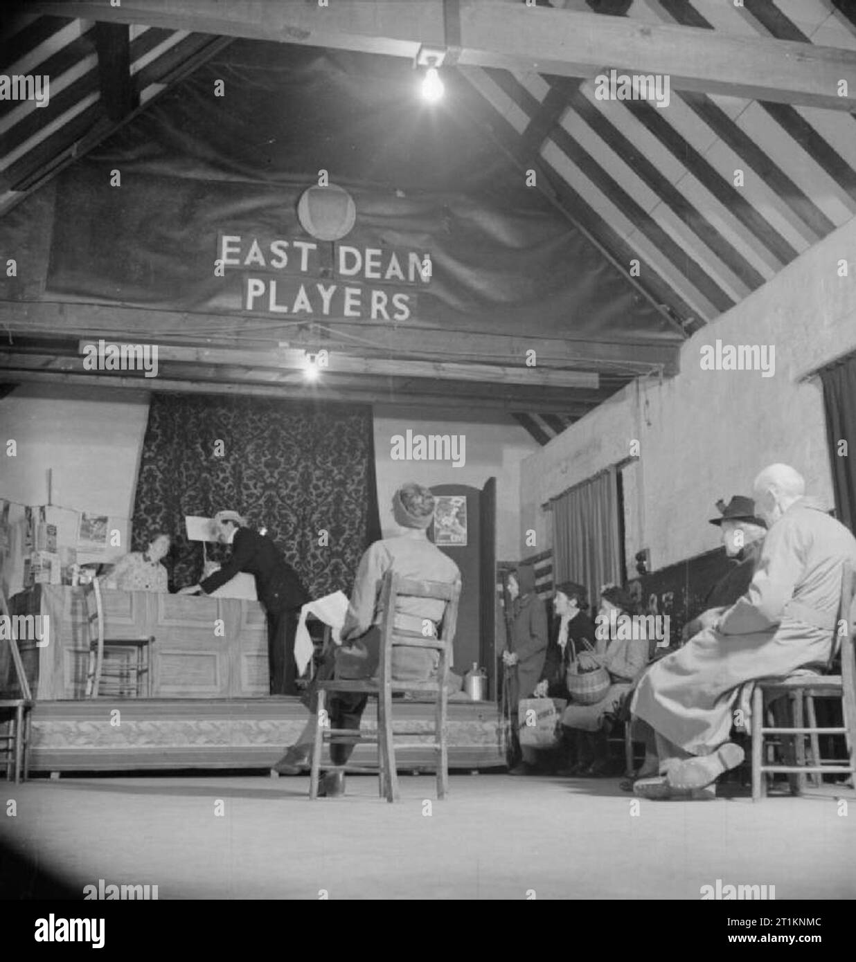 Onorevole Bugler va alla guerra - La vita quotidiana in Oriente Dean, Sussex, Inghilterra, 1943 nel villaggio hall a oriente il Decano, gli abitanti del villaggio stanno mettendo su una prestazione del gioco "troppo molte mogli'. Gli attori sulla scena sono Ray Kemp e onorevole Waffenden. Dirigere il gioco è il signor Wynne, visto qui con lei torna alla fotocamera, guardare l'azione. Molti altri abitanti del villaggio, tra cui la onorevole Bugler e onorevole Russell, (che ha recitato nel gioco come la signora Brown), si può osservare guardando le prove. La compagnia di teatro è noto come "l'Oriente Dean giocatori'. Foto Stock