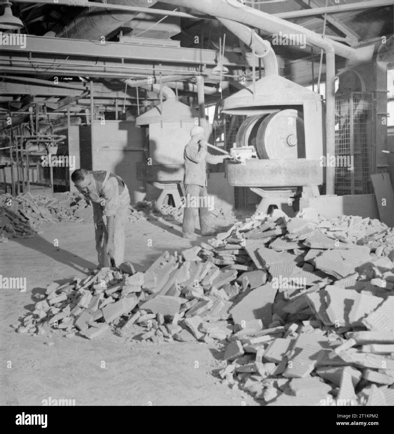 Terraglie nel rendere- il lavoro di J e G Meakin ceramiche, Hanley, Stoke-on-Trent, Staffordshire, Inghilterra, 1942 torte di argilla essendo shovelled in una smerigliatrice ad una fabbrica di ceramiche, da qualche parte in Gran Bretagna. I dolci sono state formate mediante il passaggio "labbro" (blended materie prime) attraverso una pressa per spremere l'acqua, lasciando questi hard torte dietro. Foto Stock