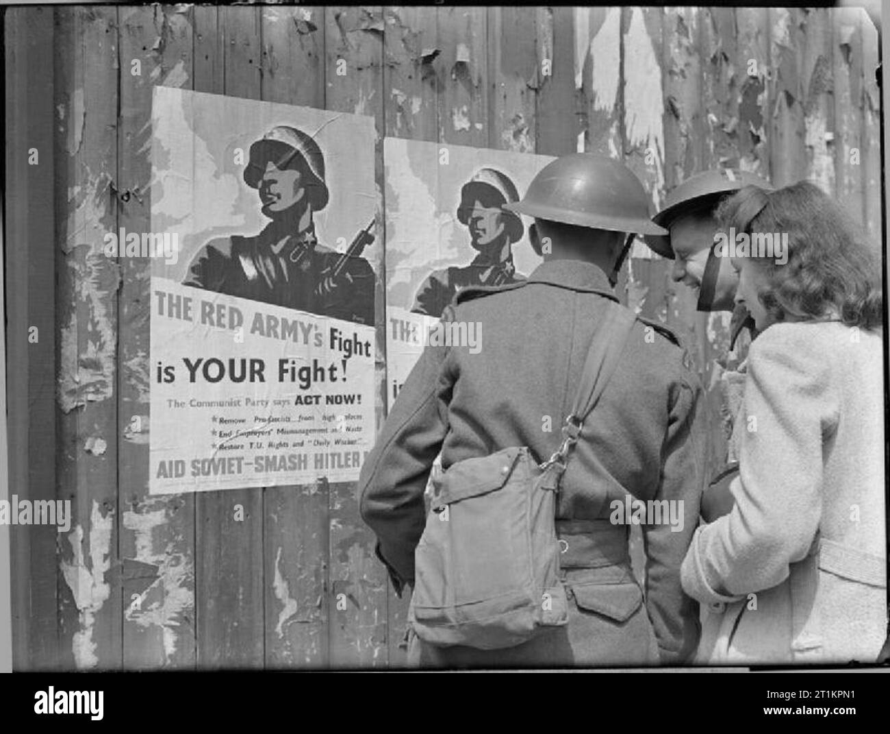 La Propaganda sulla British Home Front, 1941 due soldati e un civile donna guarda uno dei due poster incollato su di un muro di recinzione o incoraggiare i cittadini a sostenere la Russia. La funzione Poster una illustrazione di un esercito rosso soldato accanto a una silhouette delle Isole Britanniche con le parole "l'esercito rosso nella lotta è la vostra lotta!". In corrispondenza del fondo del poster sono le parole 'Aiuto Smash sovietica Hitler!". Foto Stock