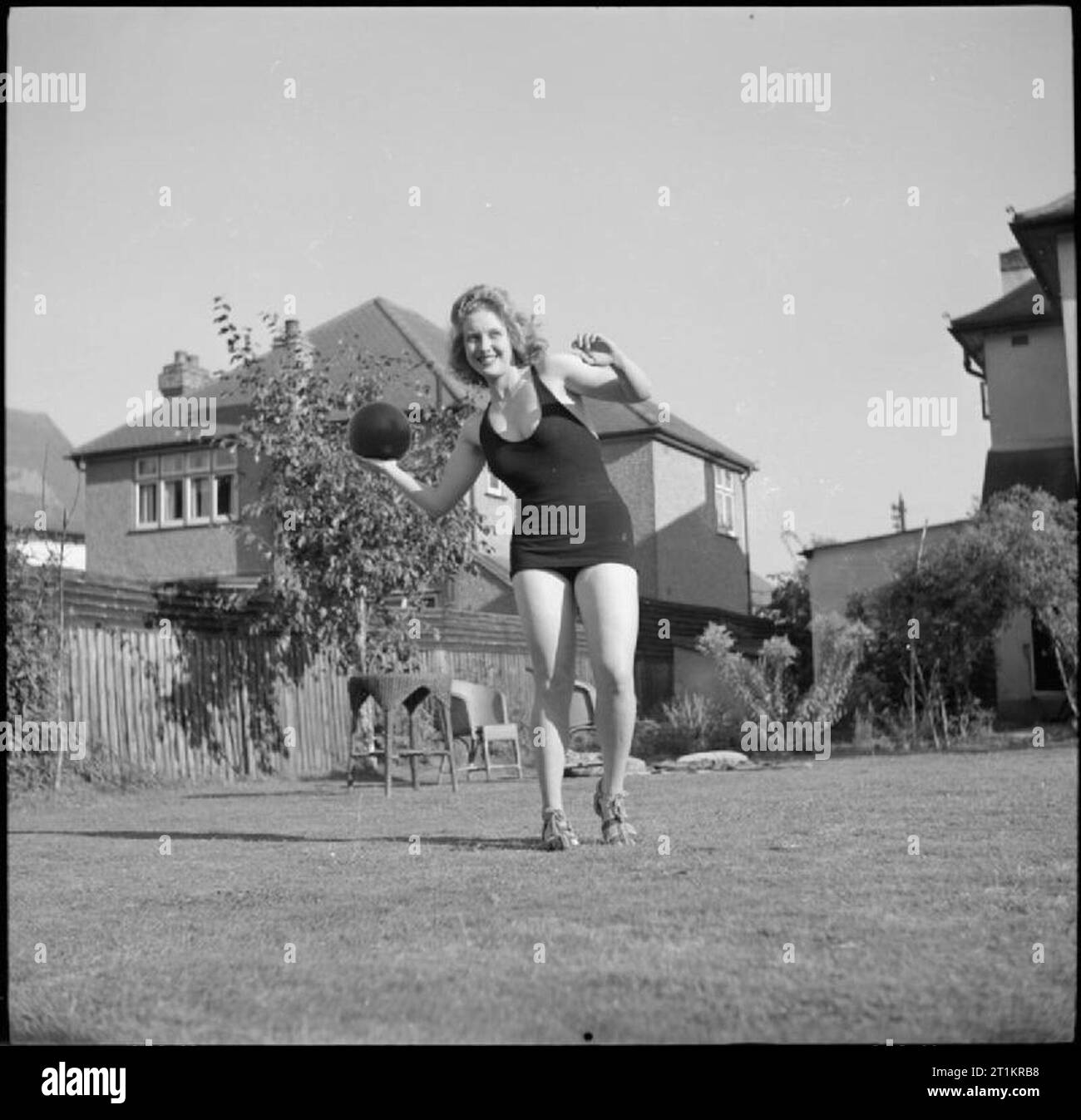 Soggiorno a Casa Vacanze - Divertimento e relax in tempo di guerra di Londra, Inghilterra, 1943 Peggy Franchi si prepara a lanciare una palla medica per la sua amica Pinkie Barnes (non raffigurata) nel giardino di casa sua, da qualche parte a Londra. Indossa un costume da bagno come i due amici sono stati a prendere il sole come parte della loro "vacanza a casa'. Foto Stock