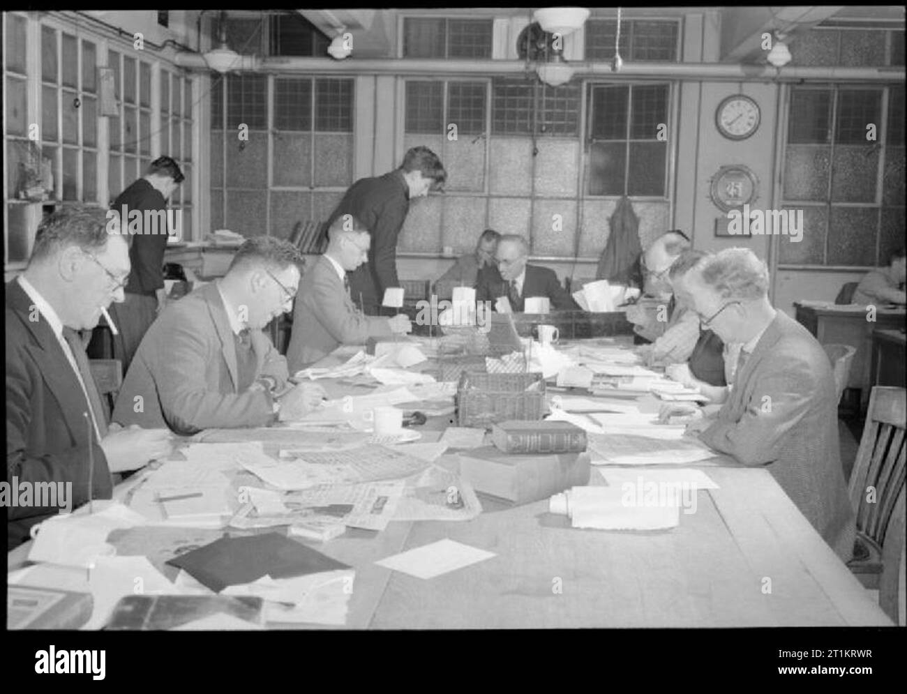 La stoffa del quotidiano moderno- Produzione di 'il Daily Mail' in tempo di guerra, Londra, Regno Unito, 1944 una trafficata scena nel sub-editor's camera presso gli uffici del quotidiano Daily Mail. Sullo sfondo al centro si può vedere Mr Taylor, Copytaster, che attraverso la legge storie (o copia) dato a lui e decide se esse sono adatte le storie e le mani sul capo sub-editor, suggerendo un particolare trattamento dell'argomento. Il tempo è di venti alle otto di sera, come indicato dal clock sulla parete in background. Foto Stock