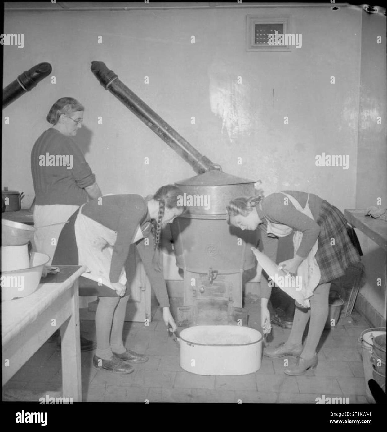 Giardini del villaggio di scolari di alimentazione- la produzione alimentare a Knighton-su-teme, Worcestershire, England, Regno Unito, 1943 sotto la supervisione del cuoco, Beryl Phillips (sinistra) e Janet Lowe raccolgono una grande pentola di patate dalla cucina per la loro scuola durante la pausa pranzo cena presso Knighton-su-teme in Worcestershire. Le verdure sono state vendute alla scuola dal villaggio locale produrre associazione, di cui Janet, il padre, un poliziotto, è un membro. Foto Stock Giardini del villaggio di scolari di alimentazione- la produzione alimentare a Knighton-su-teme, Worcestershire, England, Regno Unito, 1943 sotto la supervisione del cuoco, Beryl Phillips (sinistra) e Janet Lowe raccolgono una grande pentola di patate dalla cucina per la loro scuola durante la pausa pranzo cena presso Knighton-su-teme in Worcestershire. Le verdure sono state vendute alla scuola dal villaggio locale produrre associazione, di cui Janet, il padre, un poliziotto, è un membro. Foto Stock