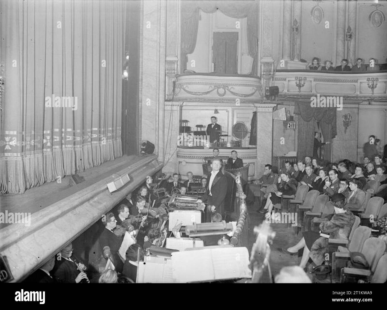 Il tempo di guerra Opera- Musica e intrattenimento presso il nuovo teatro, St Martin's Lane, London, England, Regno Unito, 1943 Le luci di casa si affievolisce e un silenzio scende oltre il pubblico, in preparazione per tenda fino al nuovo teatro, St Martin's Lane, Londra. Peter Gellhorn si prepara a condurre l'ouverture da "La Traviata". La fossa dell'orchestra presso il nuovo Teatro non è grande abbastanza per ospitare l'intero complesso, così i tamburi sono alloggiati in una scatola su un lato dello stadio (chiaramente visibile al centro della fotografia) e l'arpa è giocato dalla casella sul lato opposto del teatro (non mostrato). Foto Stock