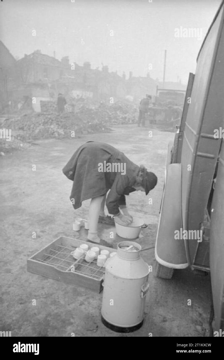 Blitz mensa- Le donne delle donne del Volontariato eseguire una mensa Mobile a Londra, Inghilterra, 1941 Pazienza "Boo' lavaggi di marca mug in un recipiente di acqua sul terreno accanto al tè WVS auto, da qualche parte a Londra, 1941. Le coppe sono lavate subito dopo l'uso e riposti in modo che essi sono immediatamente pronti quando il tè auto arriva alla sua destinazione successiva. In background, bomba-case danneggiate e pile di detriti può essere visto. Foto Stock
