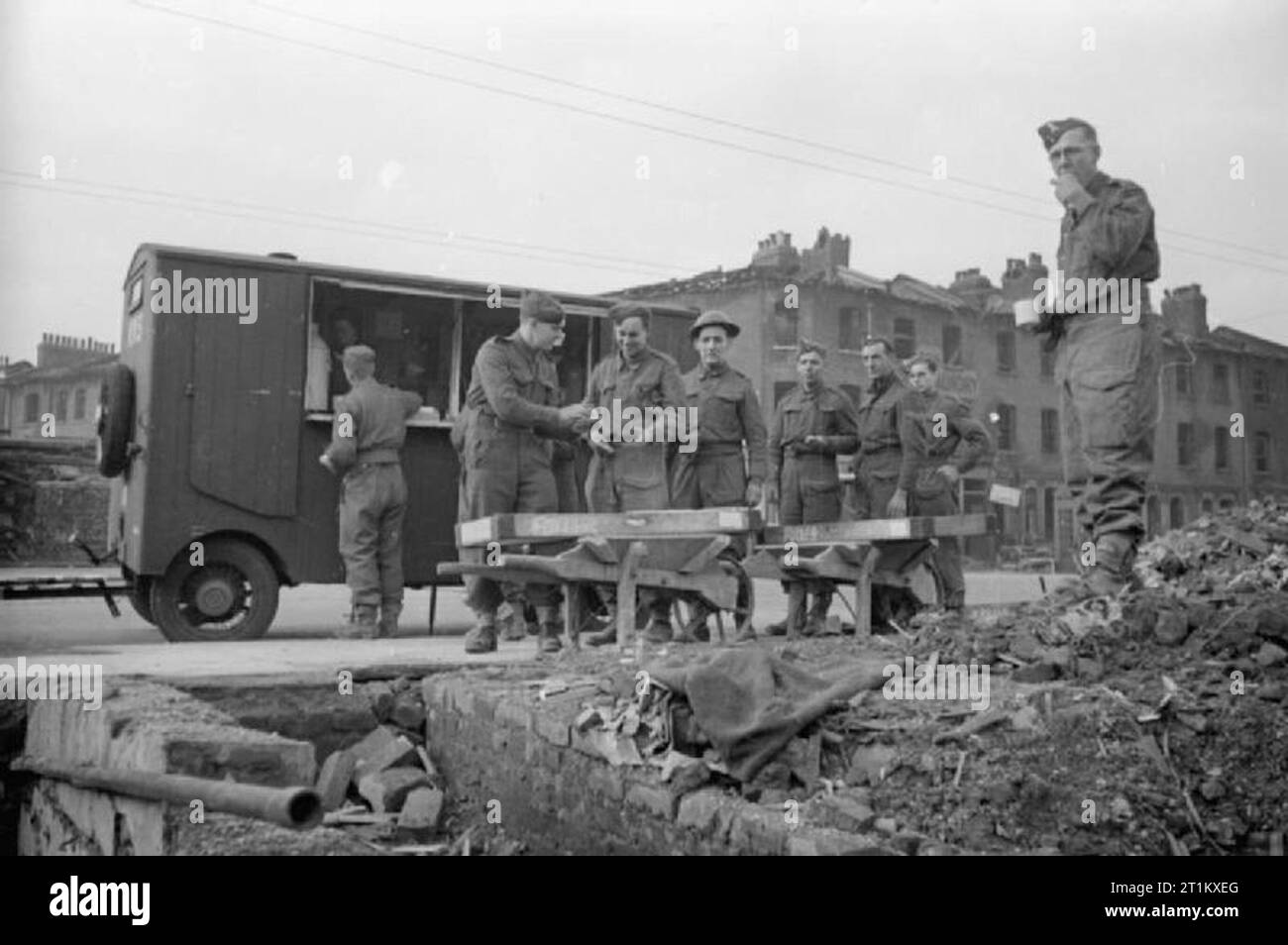 Blitz mensa- Le donne delle donne del Volontariato eseguire una mensa Mobile a Londra, Inghilterra, 1941 uomini della Pioneer Corps mangiare panini e bere il tè al fianco di una mensa WVS durante il loro mezzogiorno giorni di pausa su una bomba sito, da qualche parte a Londra. La foto è stata scattata dal sito di una casa che è stata completamente distrutta durante il raid. Più di bomba-case danneggiate, di cui uno con un segno per "Lloyd's Servizio lavanderia' può essere visto in background. Foto Stock
