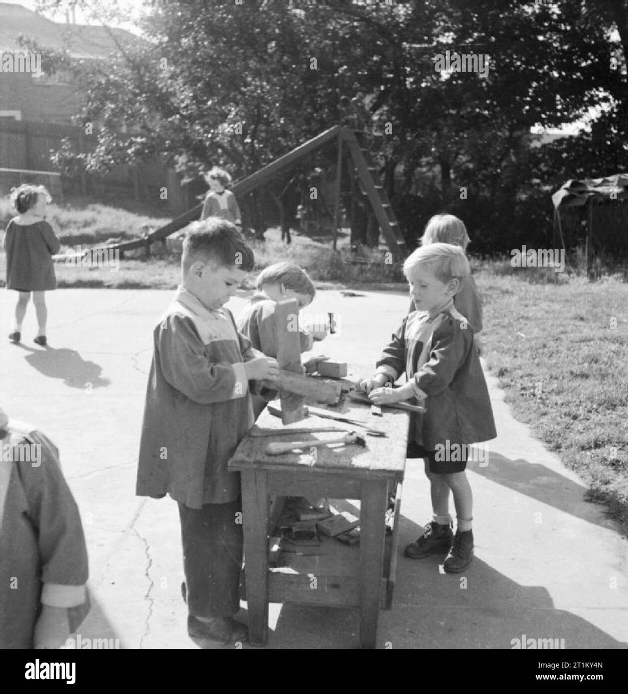 Un modello di scuola dell'infanzia- il lavoro della terra Tarner scuola materna, Brighton, Sussex England, Regno Unito, 1944 ragazzi a terra Tarner Scuola materna a Brighton godetevi una "lezione" in legno e falegnameria in corrispondenza di un banco in aria aperta della scuola parco giochi. Dietro di loro, sotto il sole, la slitta può essere visto. Foto Stock