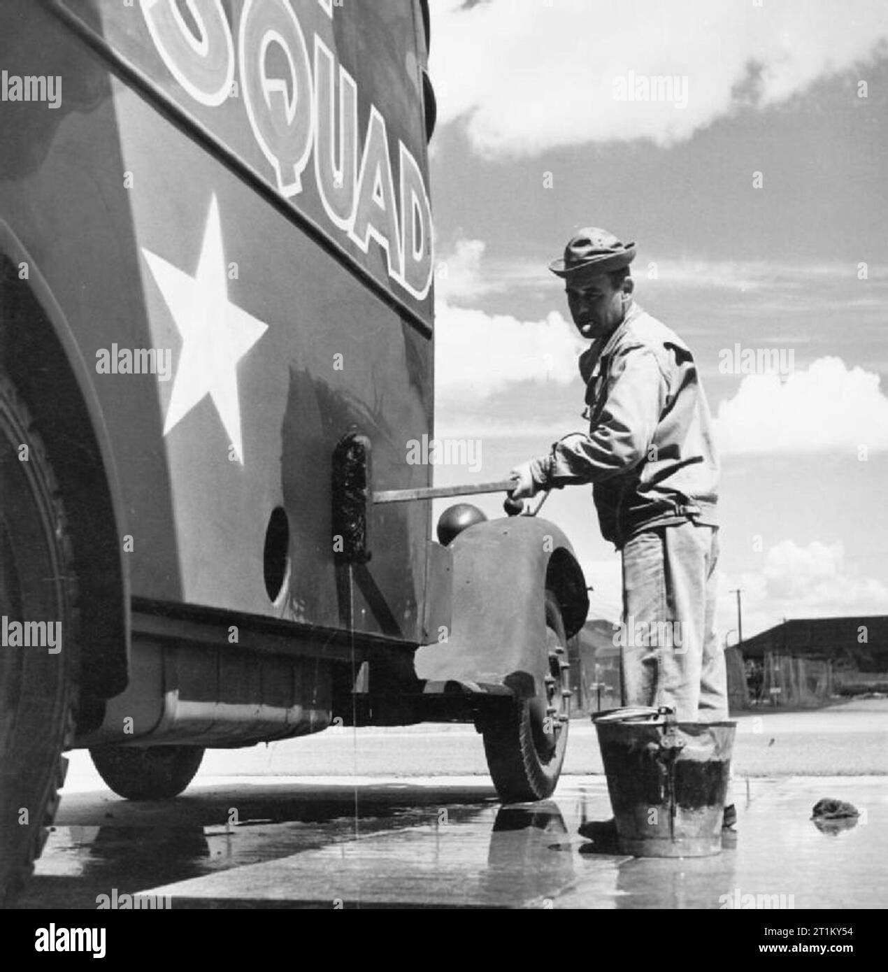 British Merci in noi le stazioni di smistamento- Anglo-american Co-operazione in tempo di guerra la Gran Bretagna, 1943 Tom Pfc Symott di 143 Baker Street, Fall River, Massachusetts fuma un sigaro come lui pulisce il lato di una ambulanza a noi cantiere di smistamento, da qualche parte in Gran Bretagna. Secondo la didascalia originale, questa ambulanza era in precedenza di proprietà dell'Esercito Britannico e vide il servizio in Francia. Esso è mantenuto dagli americani per l'uso in caso di air raid o altre situazioni di emergenza, ma ha fortunatamente non è ancora stato utilizzato. Foto Stock