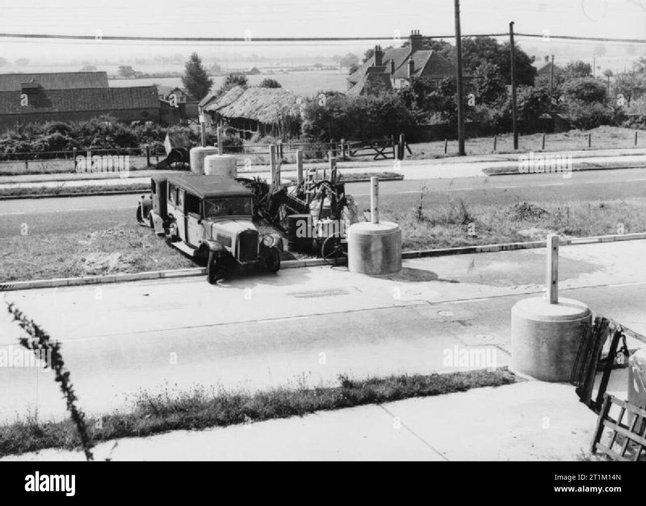 La parte anteriore di casa in Gran Bretagna durante la Seconda Guerra Mondiale una serie di blocchi di cemento contribuire a formare una diga da qualche parte in Inghilterra, 1940. Rottami di ferro e ruggine farm machinery forniscono il resto della barricata. Due vecchie autovetture sedere sulla centrale di prenotazione della strada, per essere spinto in posizione per completare il blocco stradale in caso di necessità. Foto Stock