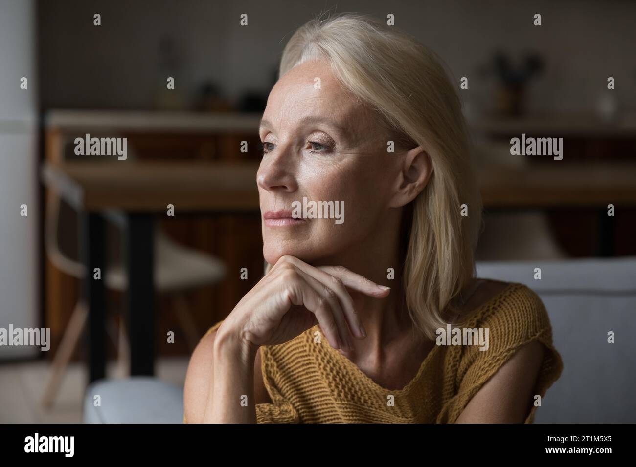 Bella e solitaria signora matura bionda seduta sul divano di casa Foto Stock