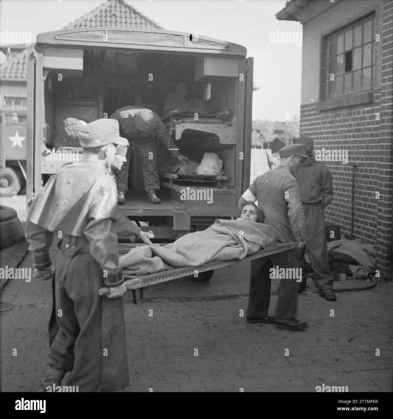 La liberazione di Bergen-Belsen Campo di Concentramento, Aprile 1945 prigionieri di guerra tedeschi e British Royal Army Medical Corps orderlies in abbigliamento protettivo scaricare prigionieri ammalati trasportati in ambulanza dal Camp n. 1 in corrispondenza della stazione di pulitura gestito da n. 7 Mobile Laboratorio batteriologico, Camp n. 2, Hohne caserma militare. La stazione di pulizia ha acquisito il soprannome di "Lavanderia umana". Foto Stock