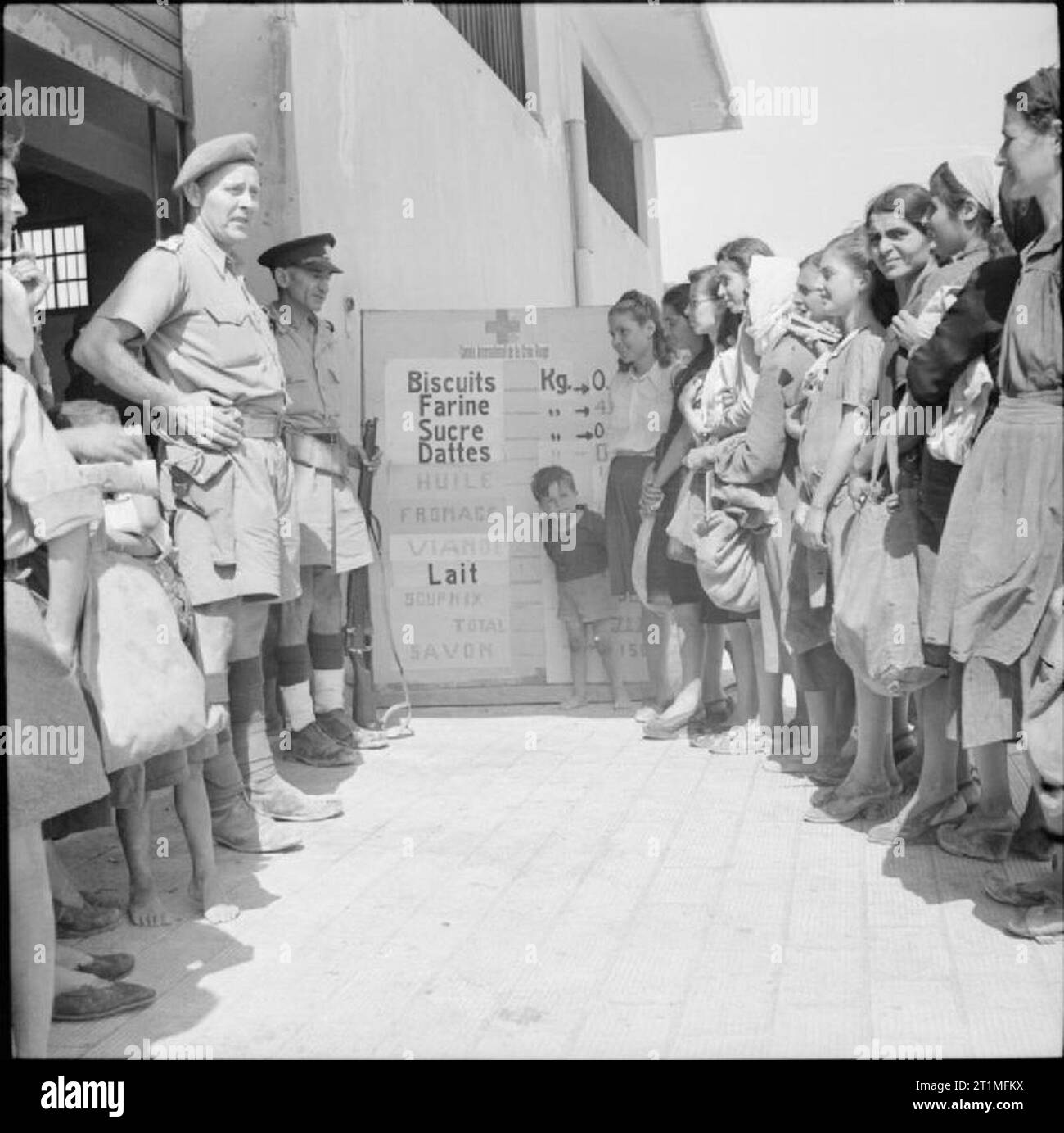 La liberazione di Rodi, 1945 civili sull'isola di Rodi per entrare in un centro di distribuzione di aiuti alimentari. A fianco del portale è una bacheca che mostra la scala di razioni alimentari ammessi per ogni persona. Durante l occupazione tedesca gli abitanti locali avevano subito gli effetti della malnutrizione a causa di insufficienza di generi alimentari. Dopo la liberazione dell'isola la British rapidamente cominciò ad organizzare le scorte di cibo, emissione di persone con razione di libri e la distribuzione di alimenti essenziali degli animali. La Croce Rossa cucine assistito anche fornendo zuppa nutriente. Foto Stock