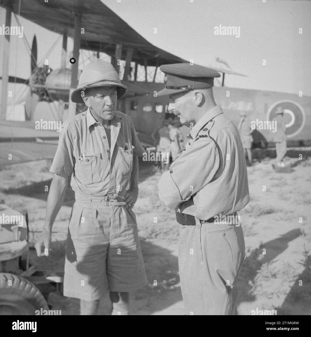 Tempo libero e divertimento durante la Seconda Guerra Mondiale il tempo di guerra animatori: Noel Coward, drammaturgo britannico e animatore con un ufficiale dell'esercito britannico che arrivano in un aeroporto per una visita per le truppe britanniche di stanza in Persia e Iraq. Noel Coward è stato uno dei pochi star intrattenitori che braved le dure condizioni di vita a visitare gli uomini della PAI [Persia e Iraq] Forza. Indossa un casco albedo con kit tropicale. Foto Stock