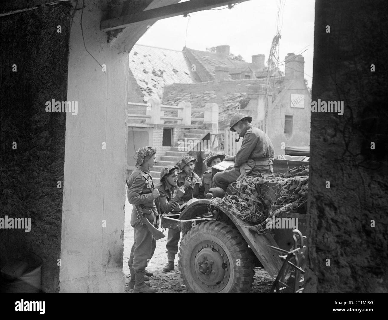 Capitano J Burgess F, Royal Artillery, briefing una parte dei telecomandi (in avanti il bombardamento di osservazione) in un villaggio della Normandia, giugno 1944. In una billetta di riposo a meno di due miglia dalla linea anteriore. Visto attraverso la porta di un edificio danneggiato capitano J Burgess F, RA, briefing il suo partito di telecomandi (in avanti il bombardamento di osservazione) prima di partire per il posto di osservazione. Il partito si muoverà fuori in un camion blindato per una certa distanza mentre il resto del viaggio è fatta a piedi. Foto Stock