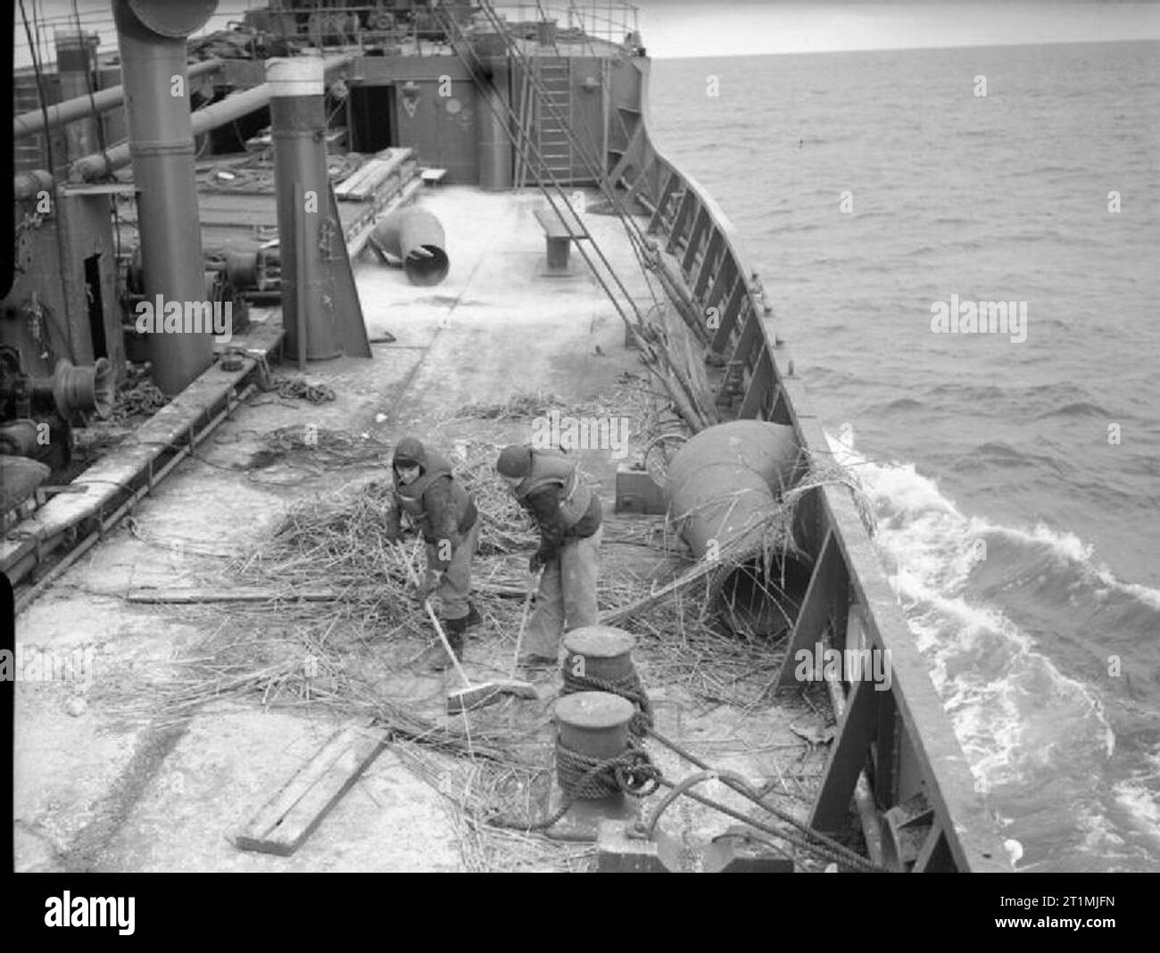 La Marina Mercantile durante la Seconda Guerra Mondiale la pulizia di ponti dopo la seconda giornata in mare a bordo della British nave mercantile EMPIRE KANGAROO in convoglio fuori della costa nord est. (Nota i due marinai sul dovere di indossare i giubbotti di salvataggio). Foto Stock