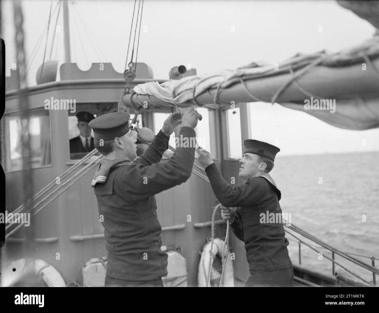 La Royal Navy durante la Seconda guerra mondiale i membri del motore di un peschereccio di equipaggio (da sinistra a destra), Ordinario Seaman J Clifford, di Liverpool, un ex rigger in tempo di pace e in grado Seaman J Gration, di Buckie, Moray Firth, un ex pescatore, che compongono la randa a bordo di uno dei navy poche navi a vela in mare nel Mediterraneo dopo aver appena completato un 2.000 miglia di viaggio dalla Gran Bretagna. Foto Stock