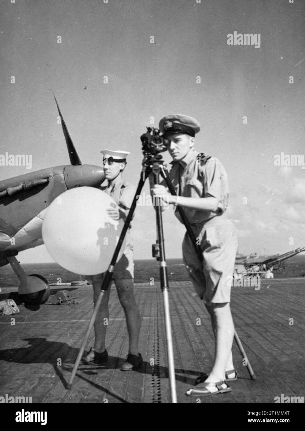 La Royal Navy durante la Seconda Guerra Mondiale in piedi accanto a un Supermarine Seafire 834 Squadrone, Fleet Air Arm, il funzionario meteorologica tenendo una vista con un palloncino pilota teodolite a bordo del escort Carrier BATTLER HMS. I barili e parte della culatta di uno dei letti 40 mm Bofors pistole possono essere visti sullo sfondo. Foto Stock