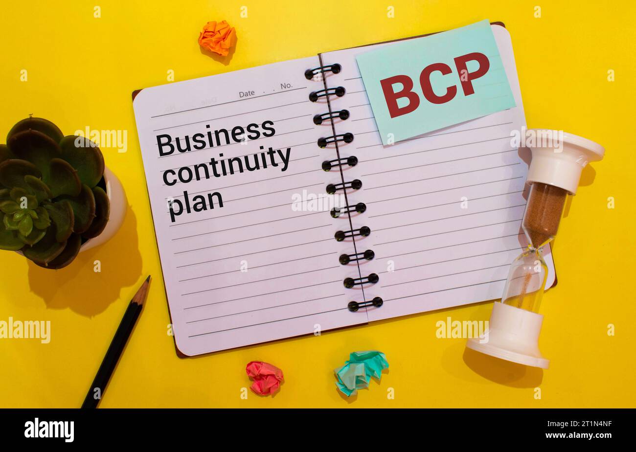 Su un tavolo da ufficio di colore chiaro si trovano un computer, una calcolatrice nera, una penna e un notebook con il testo BCP Business Continuity Plan. Foto Stock