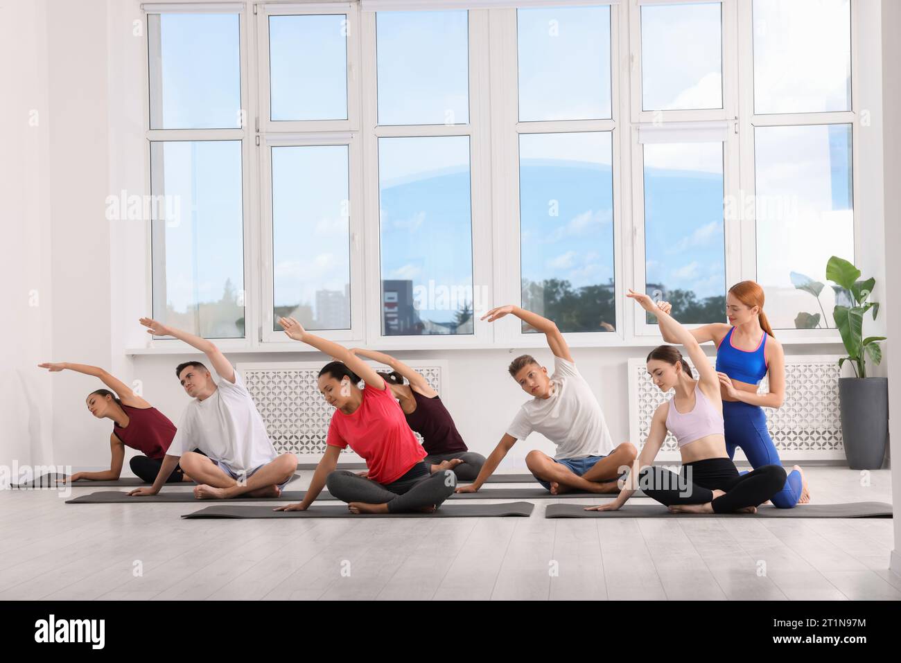 Allenatore di yoga che aiuta le donne durante le lezioni di gruppo al chiuso Foto Stock