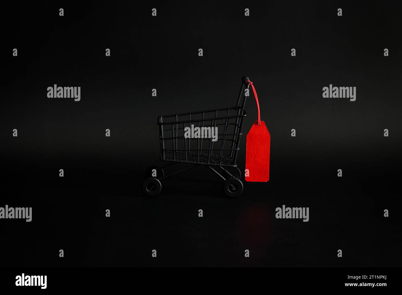 Carrello per shopping nero con cartellino di prezzo bianco rosso su sfondo nero per il concetto di vendita per lo shopping del Black Friday. Foto Stock