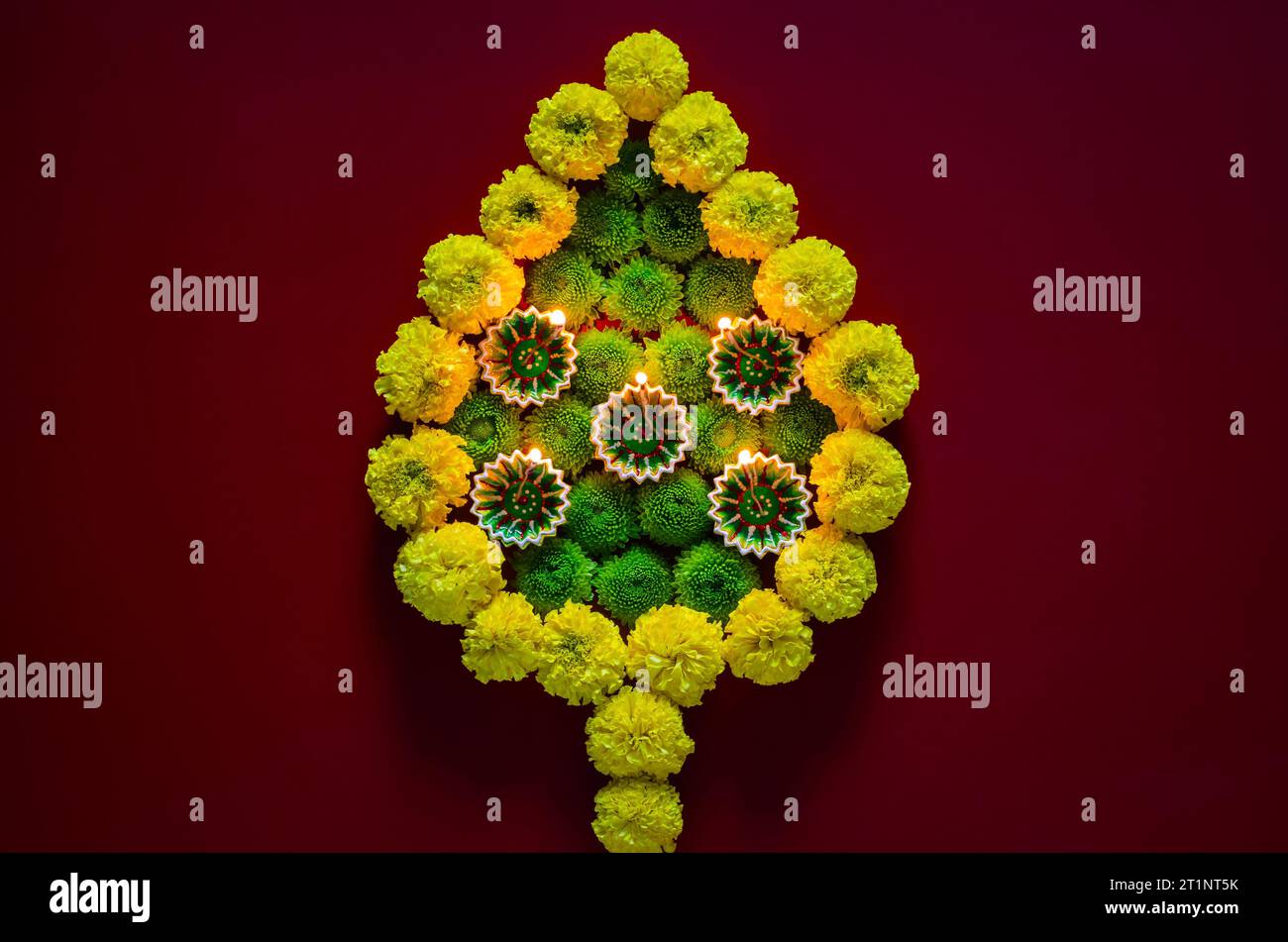 Lampade diya in argilla accese per celebrare il festival Diwali con fiori colorati a forma di fiamma su sfondo rosso scuro. Foto Stock