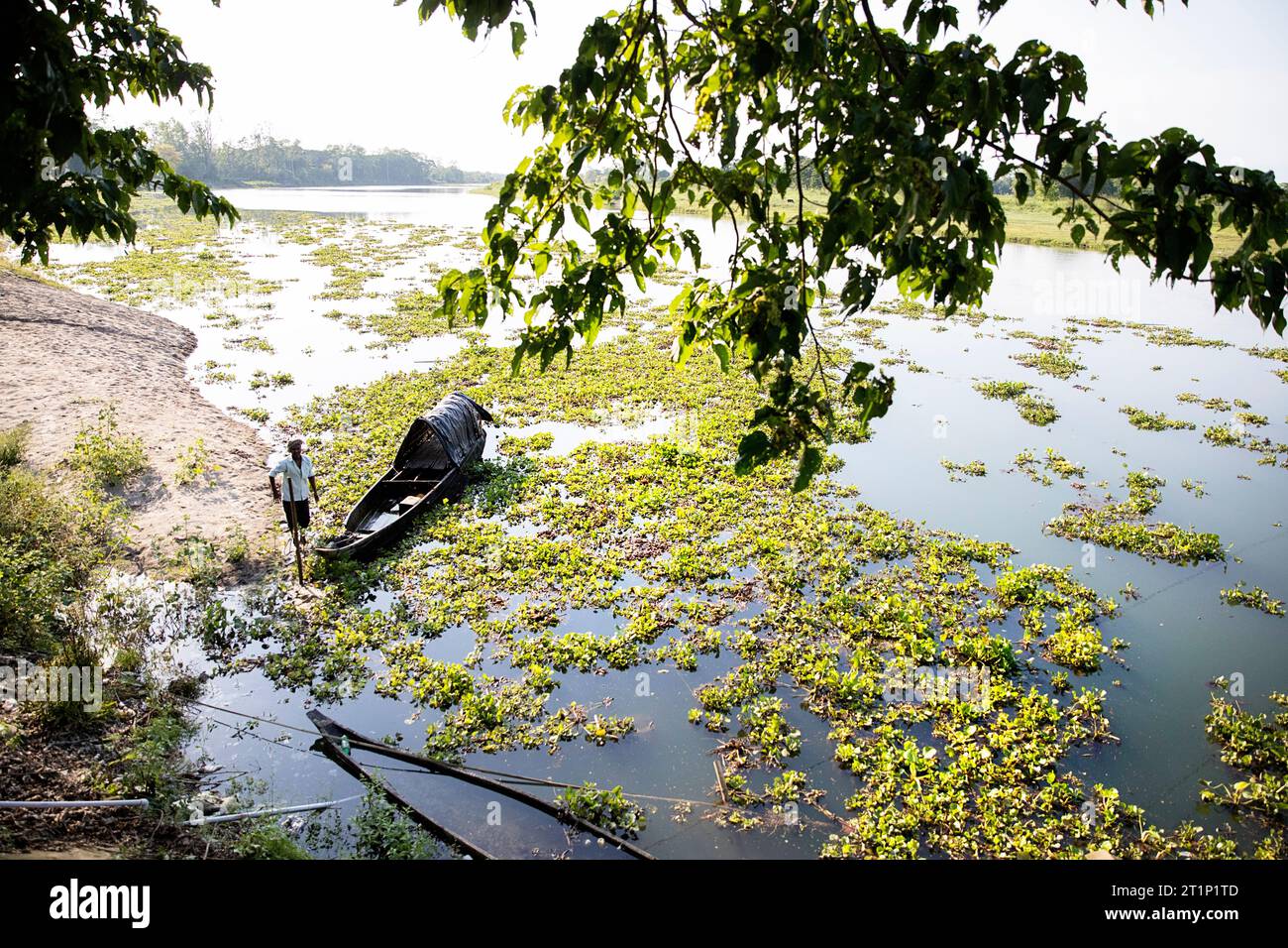 Il pescatore locale si trova su una riva di un fiume vicino alla sua tradizionale barca da pesca in legno nell'isola Majuli in india Foto Stock