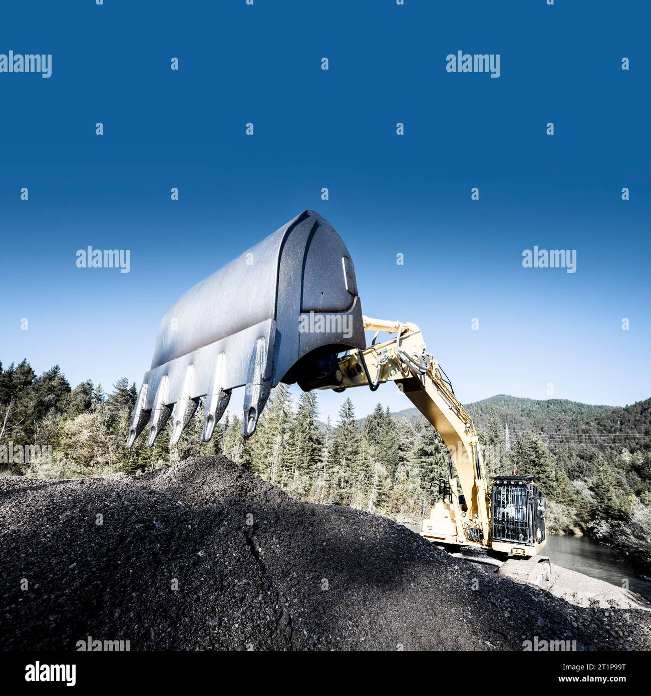 Grande escavatore a catena che draga un laghetto di stoccaggio nelle Alpi boscose sotto un cielo blu autunnale Foto Stock