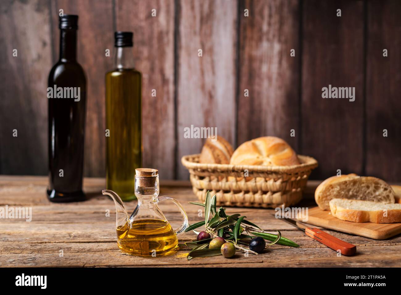 Brocca con olio d'oliva vergine accanto ad un ramo d'oliva con olive, pane di fondo e alcune bottiglie di olio d'oliva. Foto Stock