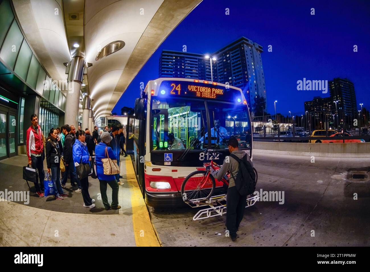 Persone che salgono a bordo di un autobus pubblico della Toronto Transit Commission nella stazione di Victoria Park. Un uomo mette una bicicletta nel portapacchi anteriore del veicolo a motore Foto Stock