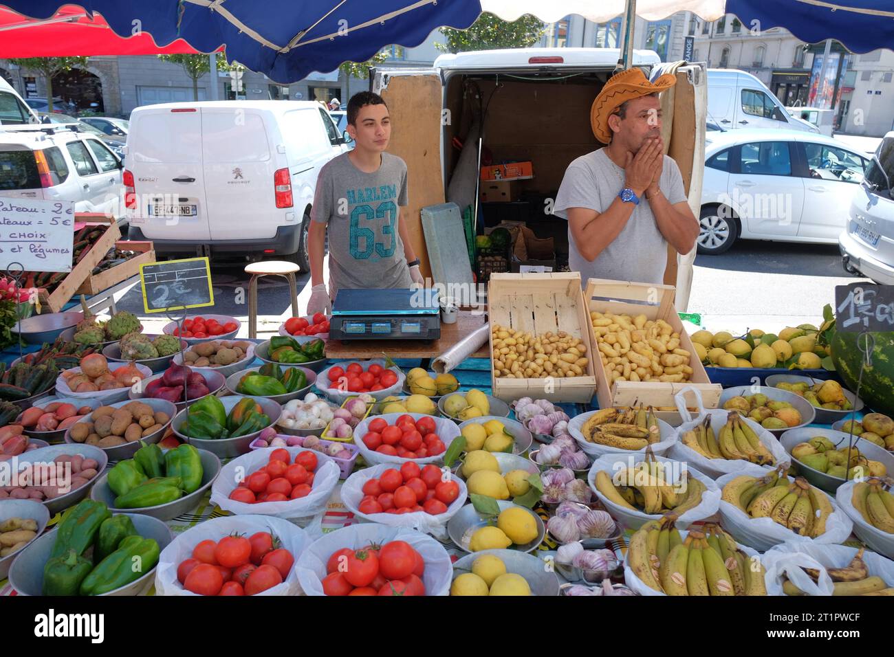 Un giovane uomo e un uomo con un cappello da cowboy di paglia lavorano su una bancarella di frutta in un mercato all'aperto a Lione, in Francia Foto Stock