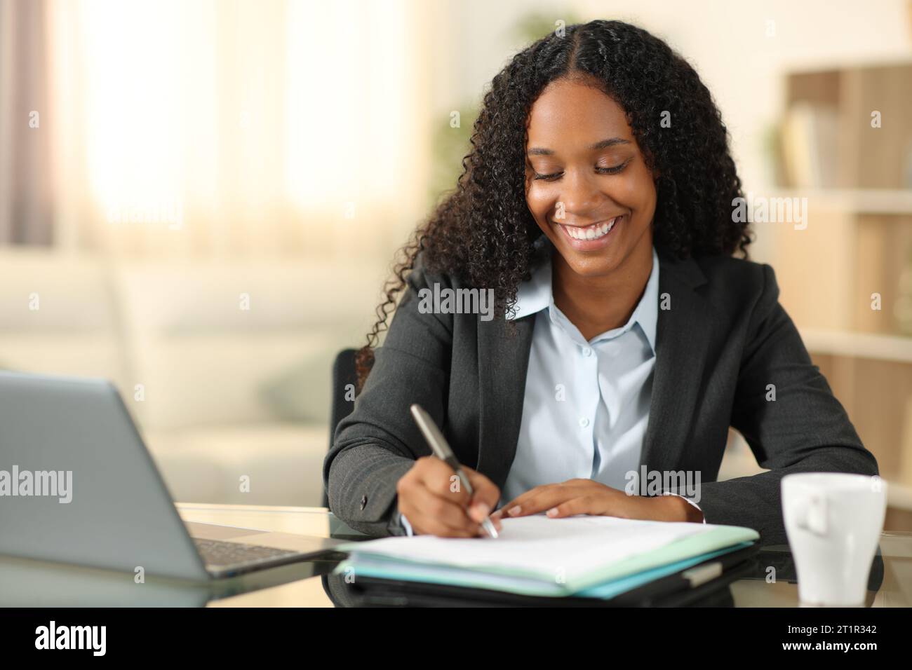 Lavoratore di teleobiettivo nero felice che compila il modulo di lavoro a casa Foto Stock