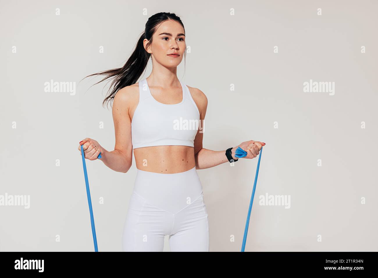 Donna in forma con abiti sportivi bianchi che si allenano con la fascia di resistenza in studio Foto Stock