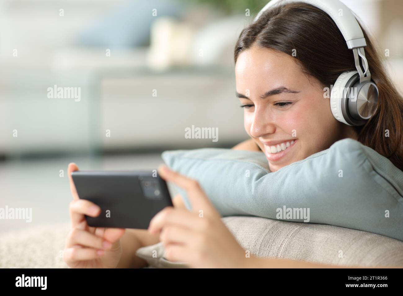 Donna felice che indossa le cuffie per guardare contenuti multimediali sullo smartphone a casa Foto Stock