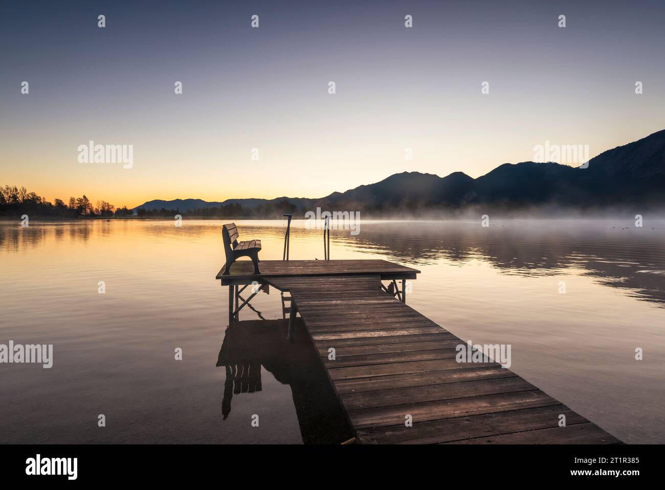 Una passerella pedonale in legno sulla riva del lago Kochel nella luce dorata dell'alba in autunno, Baviera, Germania Foto Stock