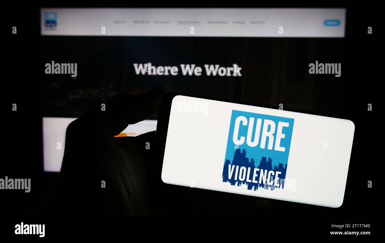 Persona in possesso di un telefono cellulare con il logo dell'organizzazione americana cure Violence Global davanti alla pagina web. Concentrarsi sul display del telefono. Foto Stock