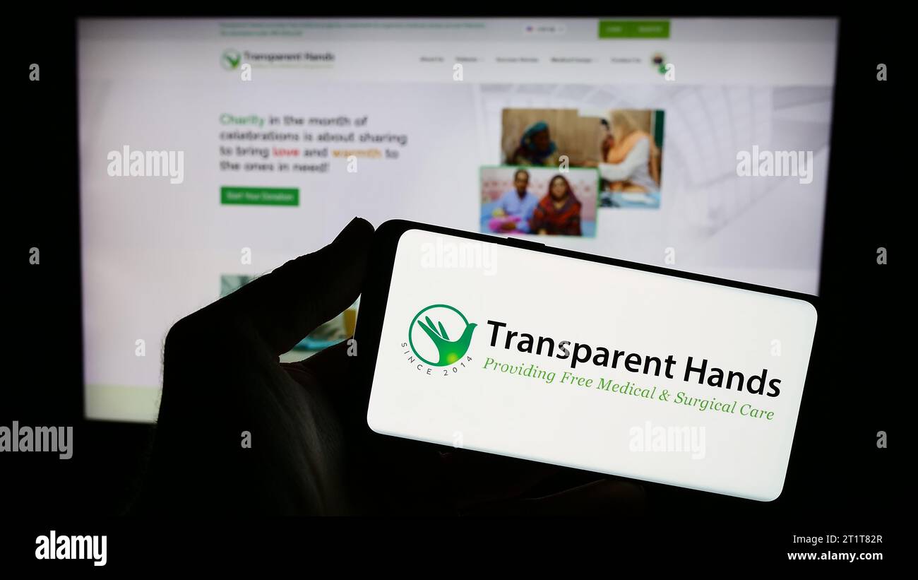 Persona che possiede uno smartphone con il logo di un'organizzazione no-profit statunitense mani trasparenti davanti al sito Web. Concentrarsi sul display del telefono. Foto Stock
