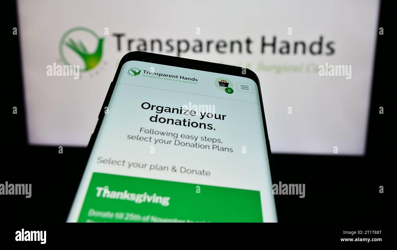 Telefono cellulare con sito Web di un'organizzazione no-profit statunitense mani trasparenti davanti al logo. Mettere a fuoco in alto a sinistra sul display del telefono. Foto Stock