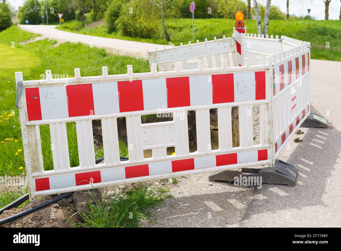 Un foro con una tubazione rotta riempita d'acqua è limitato da una recinzione temporanea per la protezione anticaduta. Recinzione di emergenza. Foto Stock