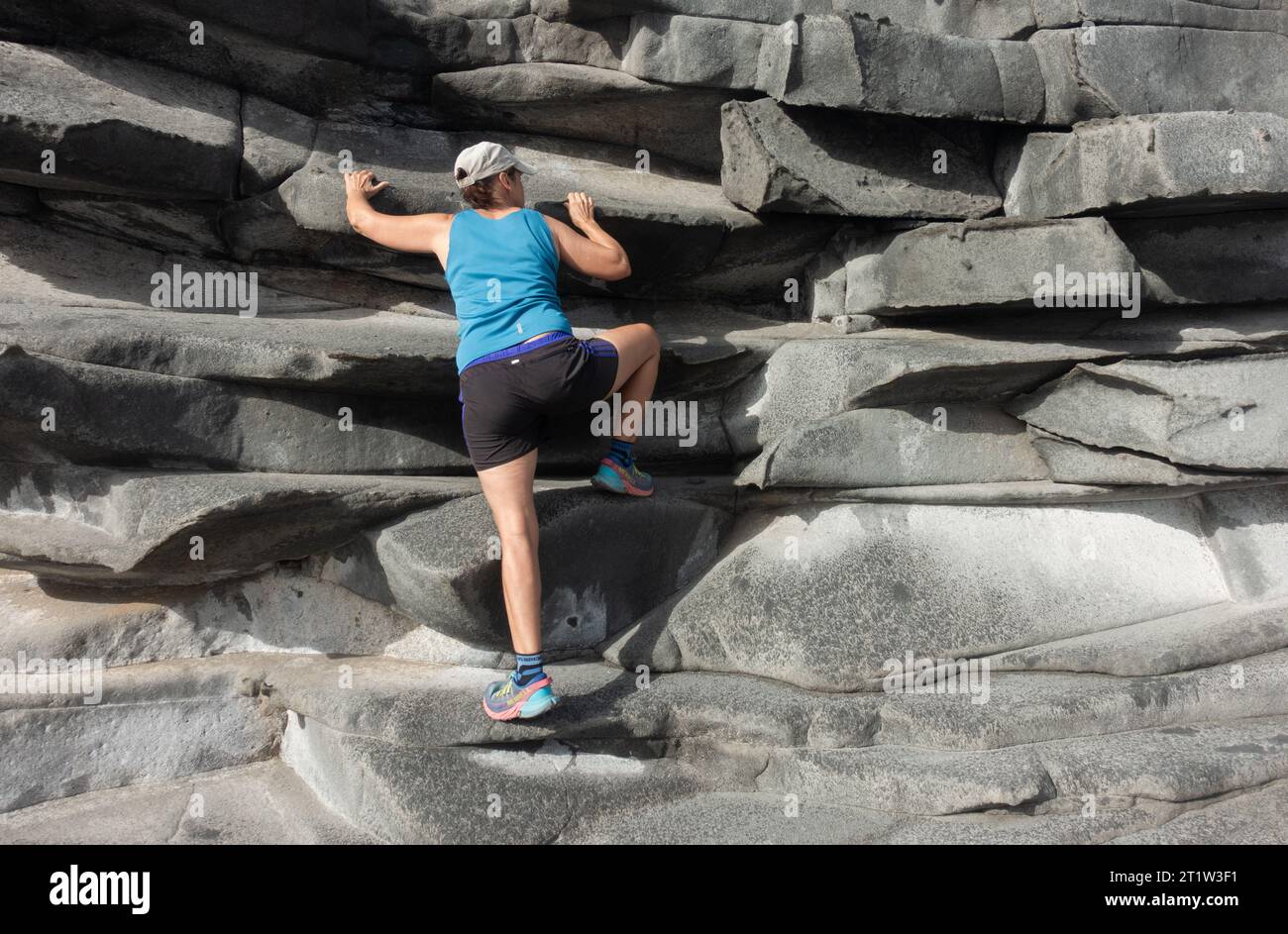 Donna che arrampica sulle rocce costiere Foto Stock
