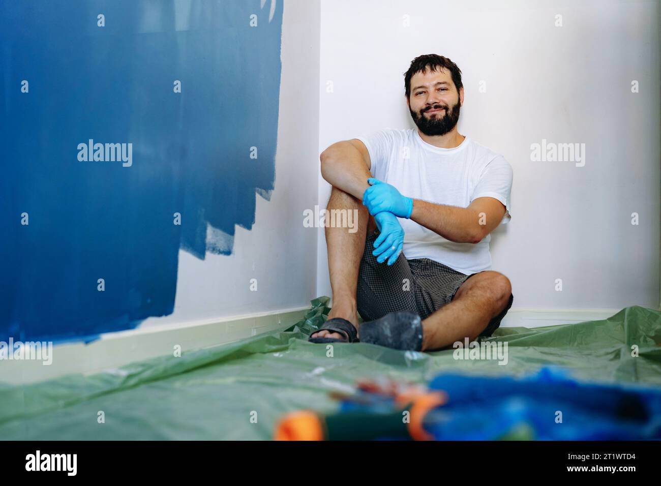 ristrutturazione della casa. Uomo barbuto caucasico che riposa dopo aver dipinto il muro immagine con messa a fuoco selettiva Foto Stock