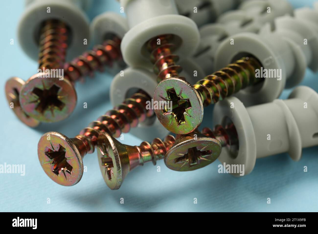 Molte viti metalliche con tasselli su sfondo azzurro, primo piano Foto Stock