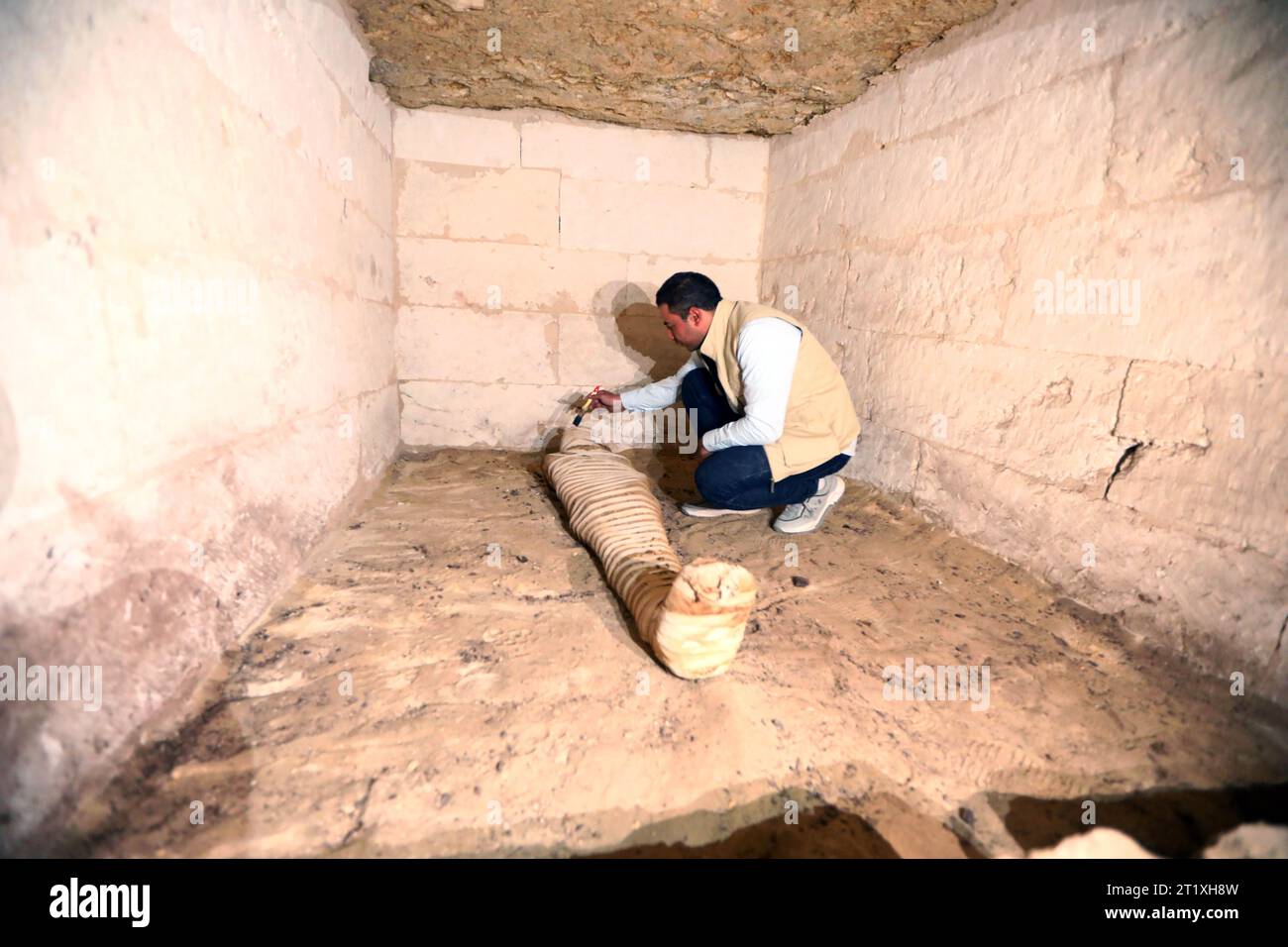 Minya, Egitto. 15 ottobre 2023. Un operaio archeologico pulisce una mummia all'interno di una tomba scavata nella roccia in un cimitero nel Governatorato di Minya, in Egitto, 15 ottobre 2023. Un cimitero risalente al nuovo Regno dell'antico Egitto è stato rinvenuto nella necropoli di Tuna El-Gebel nel governatorato di Minya, nel sud dell'Egitto, il Ministero egiziano del Turismo e delle Antichità annunciato domenica. Credito: Ahmed Gomaa/Xinhua/Alamy Live News Foto Stock