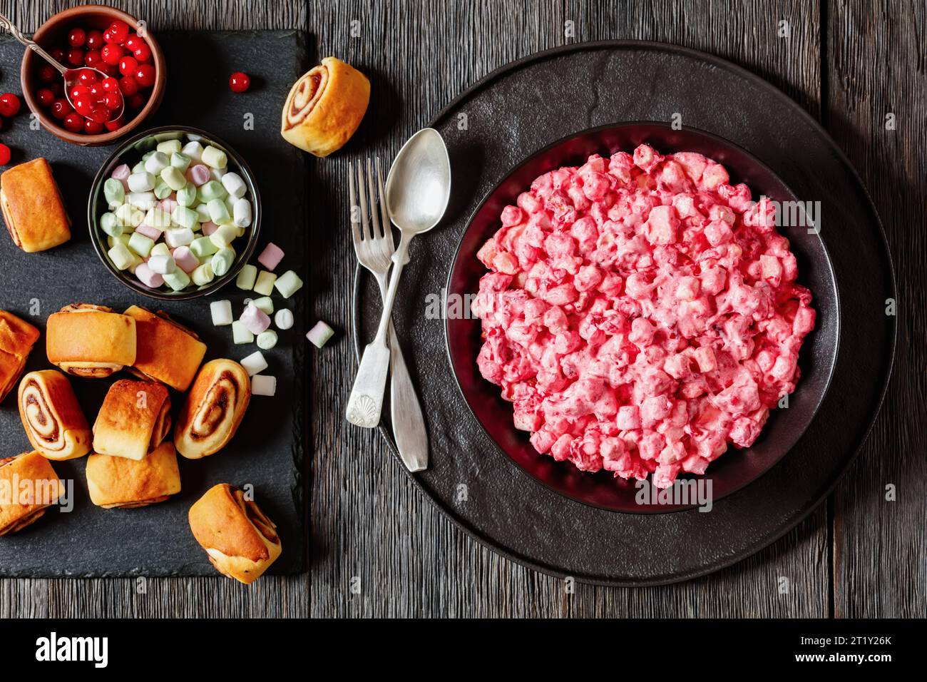 insalata cremosa di mirtilli rossi con mini marshmallow, mela fresca e noci pecan in ciotola nera su tavolo di legno scuro con panini alla cannella, ricetta americana, ho Foto Stock