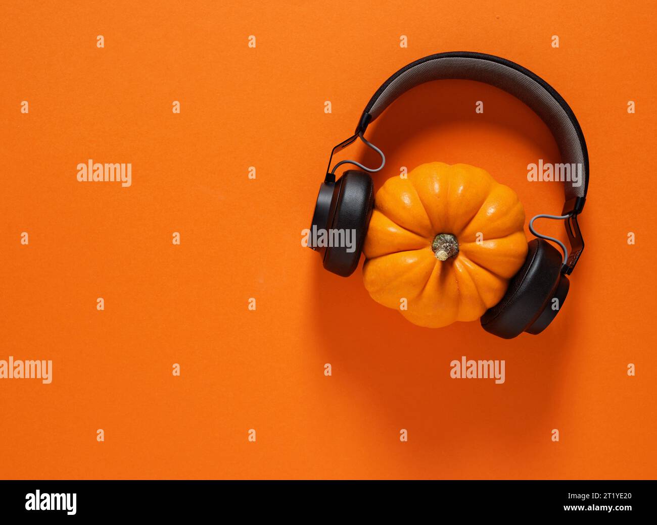 Concetto di festa di Halloween. Zucca autunnale con cuffie wireless nere su sfondo arancione con spazio per la copia. Foto Stock
