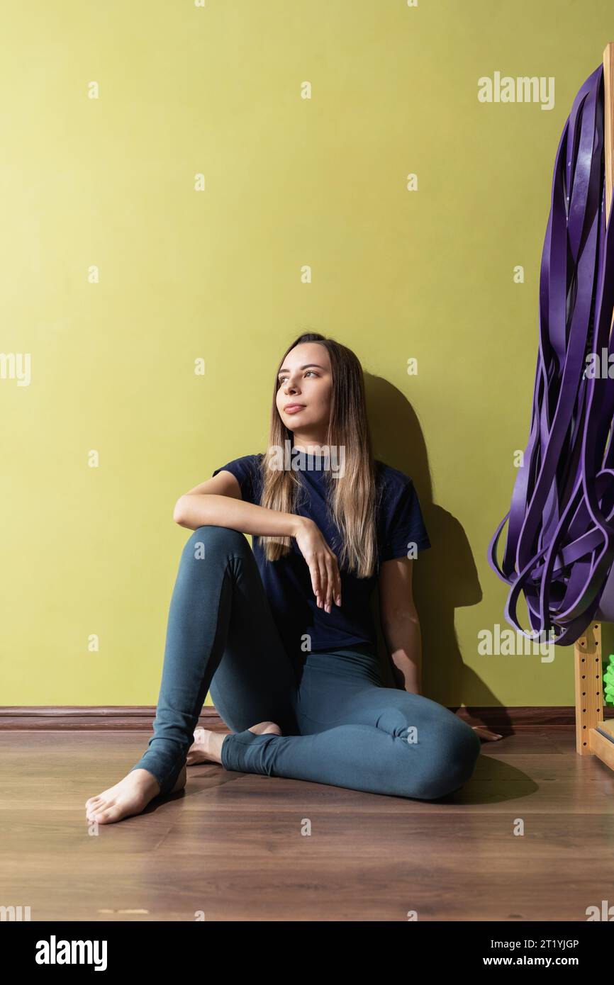 Ritratto a figura intera di una giovane donna seduta vicino a una parete in abbigliamento sportivo e riposante dopo un allenamento nella sala fitness Foto Stock