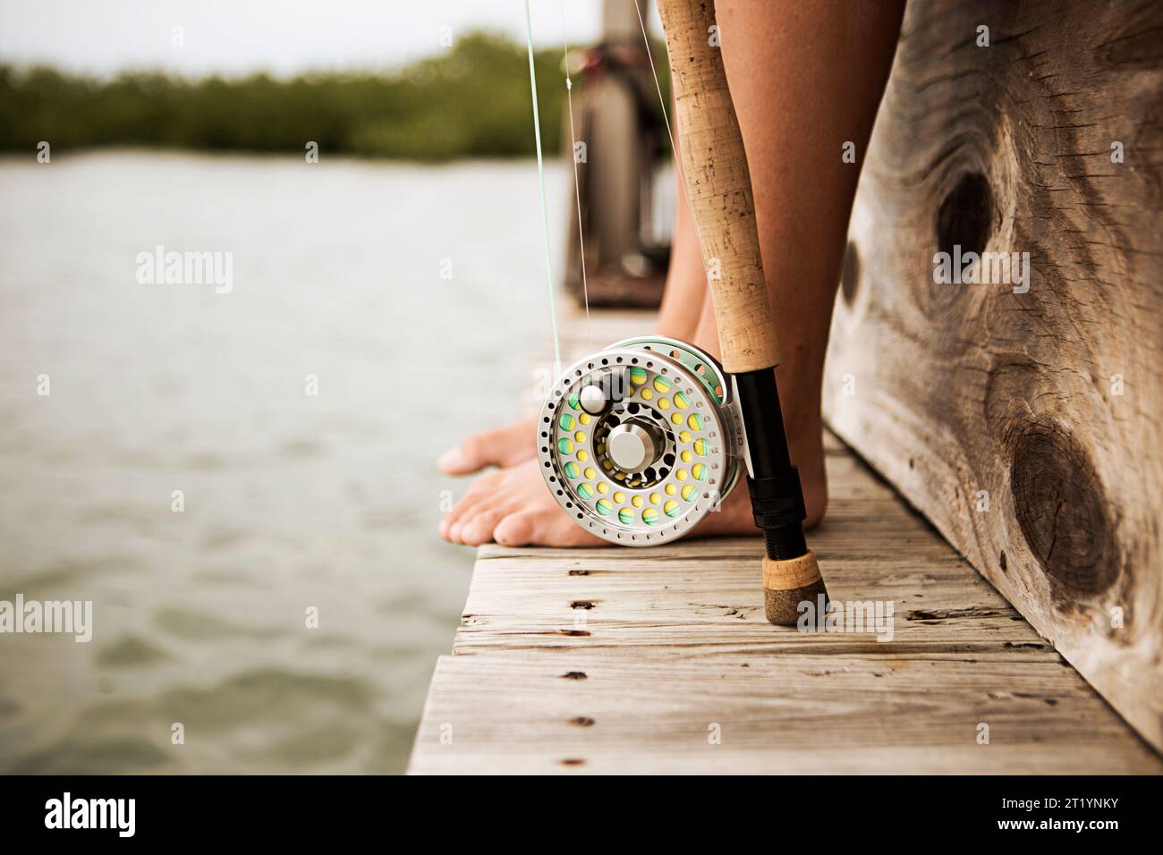 Canna da pesca e piedi di donna sul molo Foto Stock