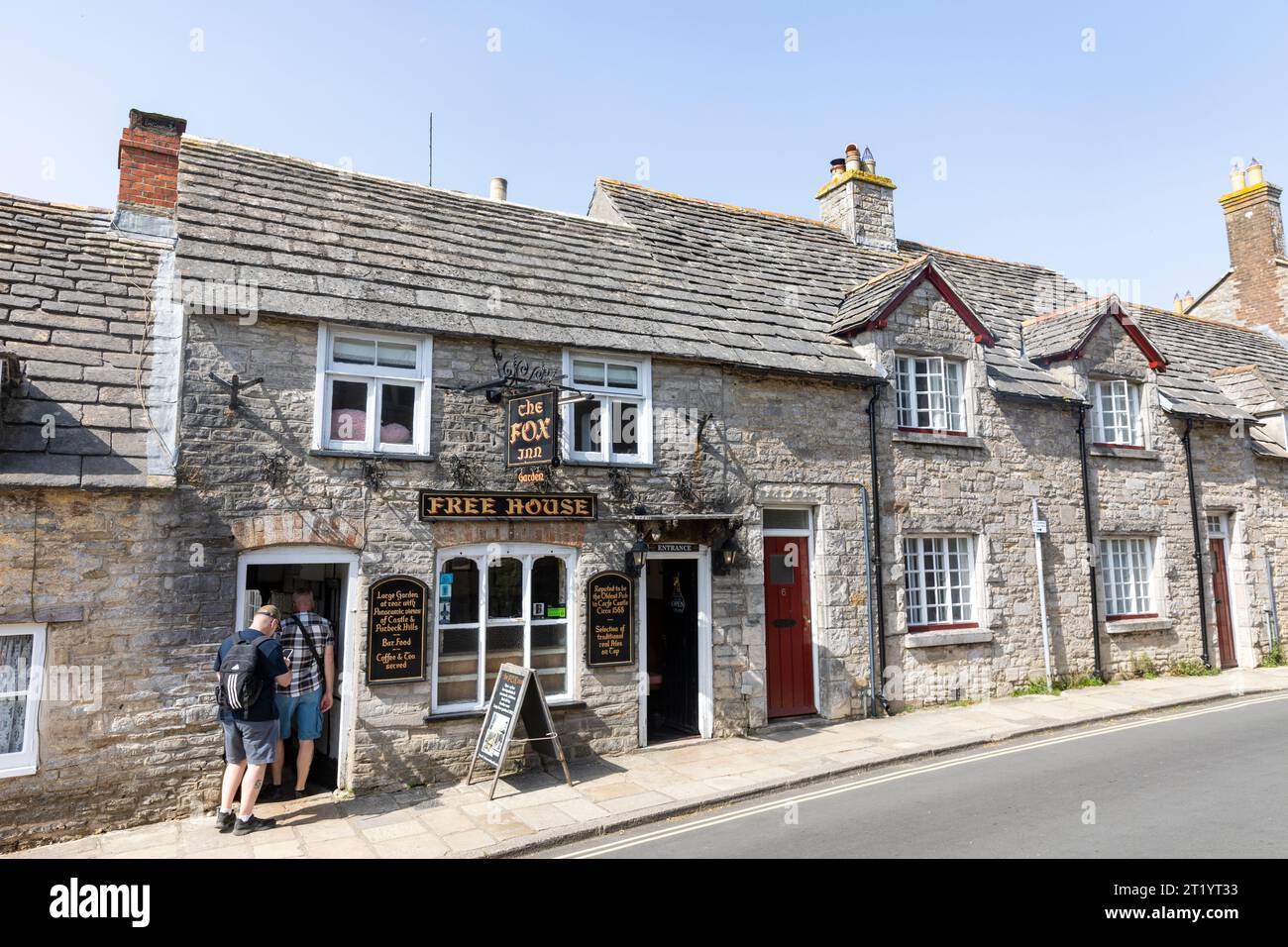 Corfe Castle nel Dorset, Inghilterra, soleggiato giorno autunnale e due uomini si dirigono verso il Fox Inn Public House in West Street, Inghilterra, Regno Unito Foto Stock