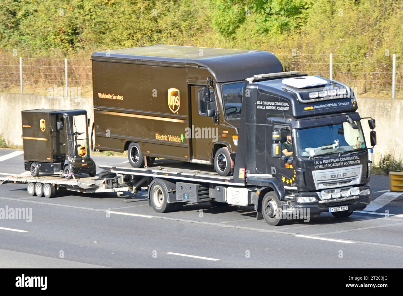 Camion di recupero con piattaforma piatta DAF caricato UPS rimorchio per il traino di furgoni pacchi elettrici che trasporta un carrello di carico UPS in miniatura su M25 Road Inghilterra Regno Unito Foto Stock
