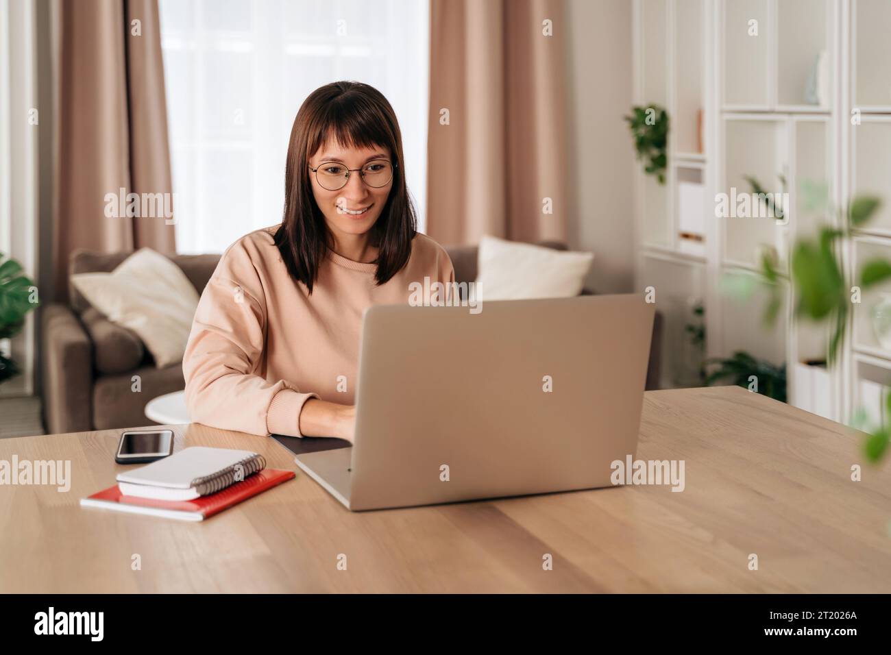 Piacevole e felice giovane donna freelance che lavora su un laptop a casa. Attraente donna d'affari che studia online, utilizza software per laptop, naviga sul Web o fa shopping online Foto Stock