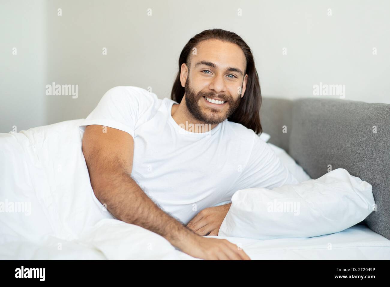 Sorridente soddisfatto uomo a pelo lungo sdraiato in un comodo letto Foto Stock