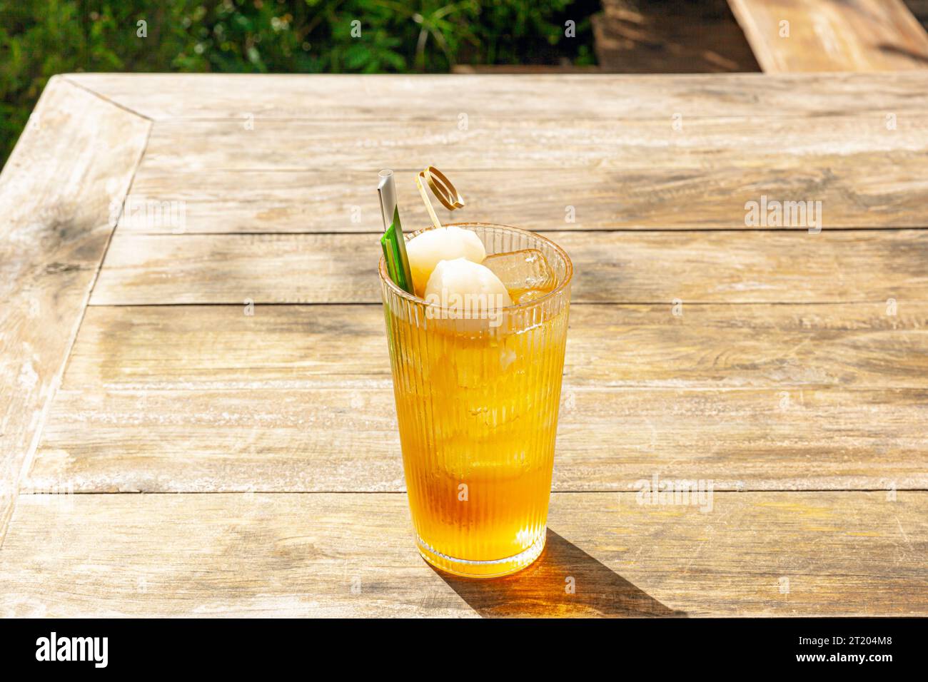 Tè fresco fatto in casa con ghiaccio Lychee con foglie di panda servito su un tavolo di legno all'aperto. bevanda estiva a base di frutta fresca nel pomeriggio soleggiato con giardino verde alle spalle Foto Stock